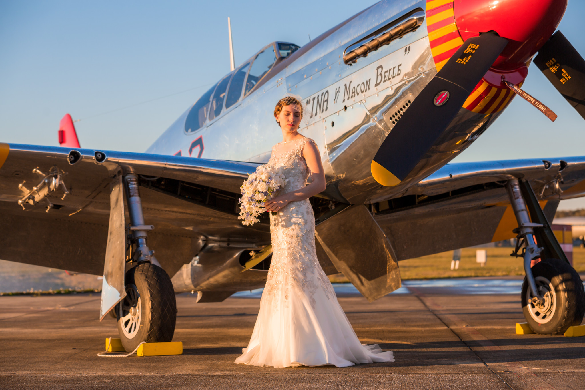 Bride in vintage wedding dress posing for pictures by WWII fighter plane