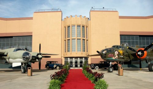 Art Deco Building Exterior with Red Carpet Military Bombers and Vintage Vehicles